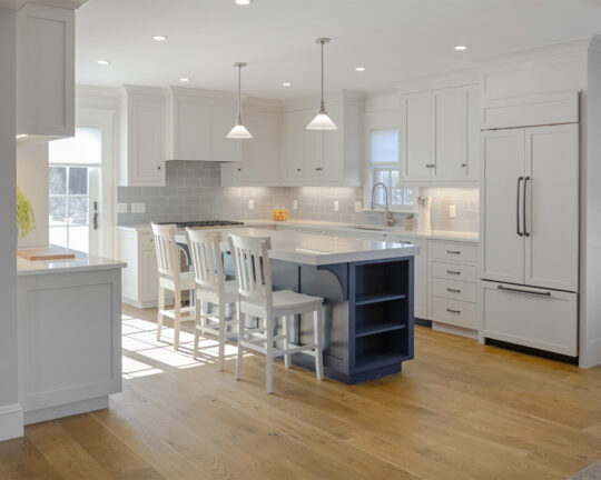 Modern, sunny kitchen with blue island, white cabinets, and chestnut colored wood floor