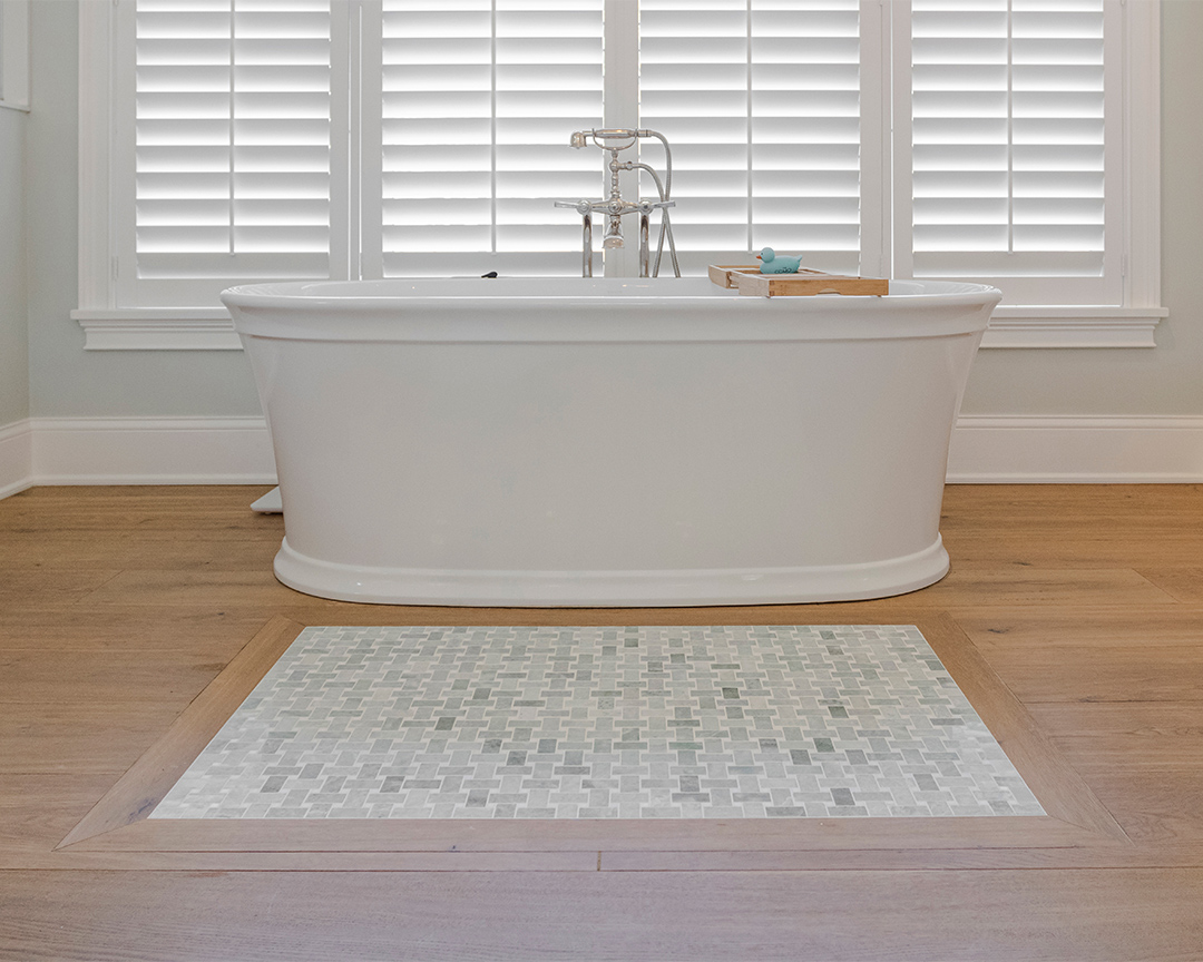 beautiful white bathtub in big bathroom with accent tile design surrounded by wide plank oak flooring