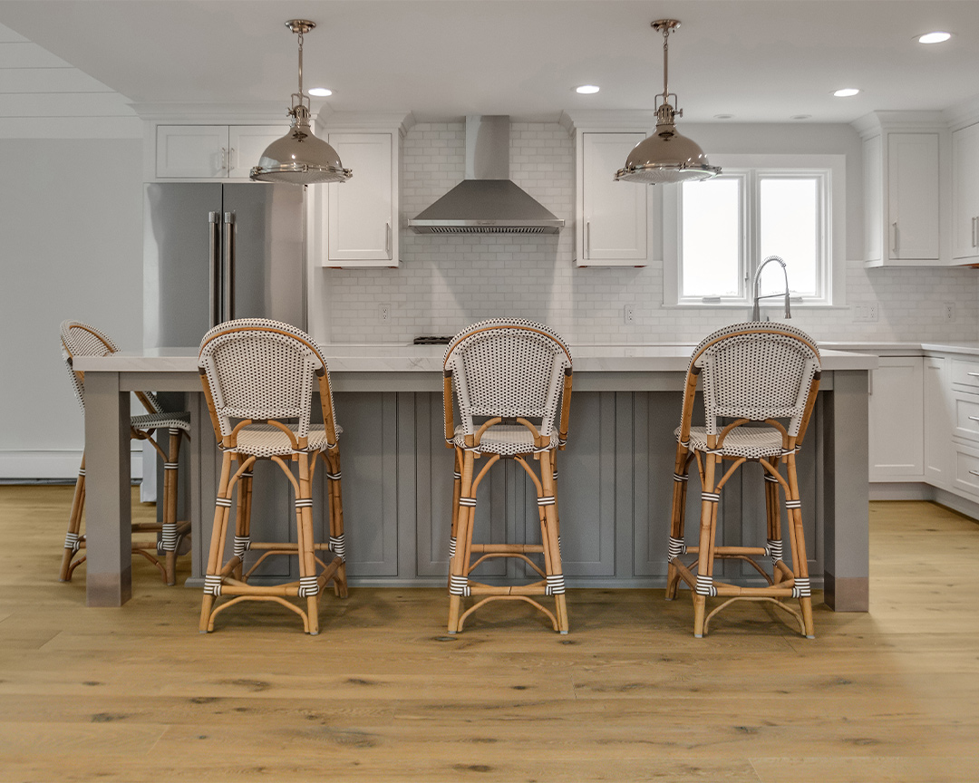 White and gray colored kitchen and island with rattan chairs and a wide plank wood floor