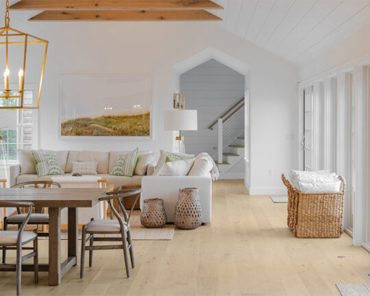 Coastal living room and dining area with decorative painting and vases, and wide plank wood floor
