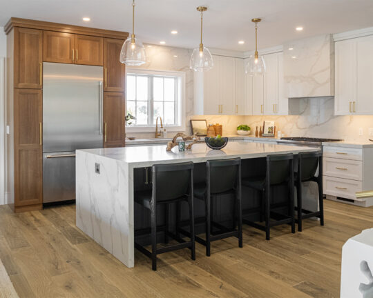 Kitchen with white cabinets and brown accents, island with dining chairs, and wide plank wood floor