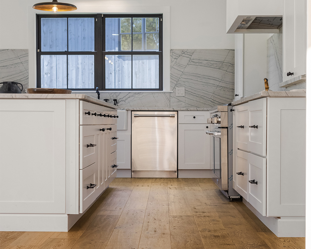 Close up of modern kitchen with white cabinets and backsplash, with rustic wood flooring