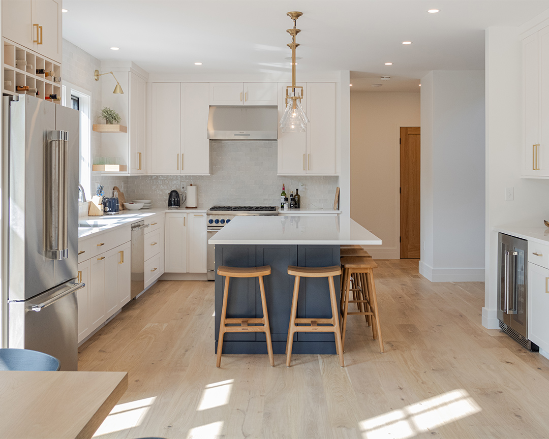 A bright kitchen with light colored unfinished flooring, white cabinets, and blue island