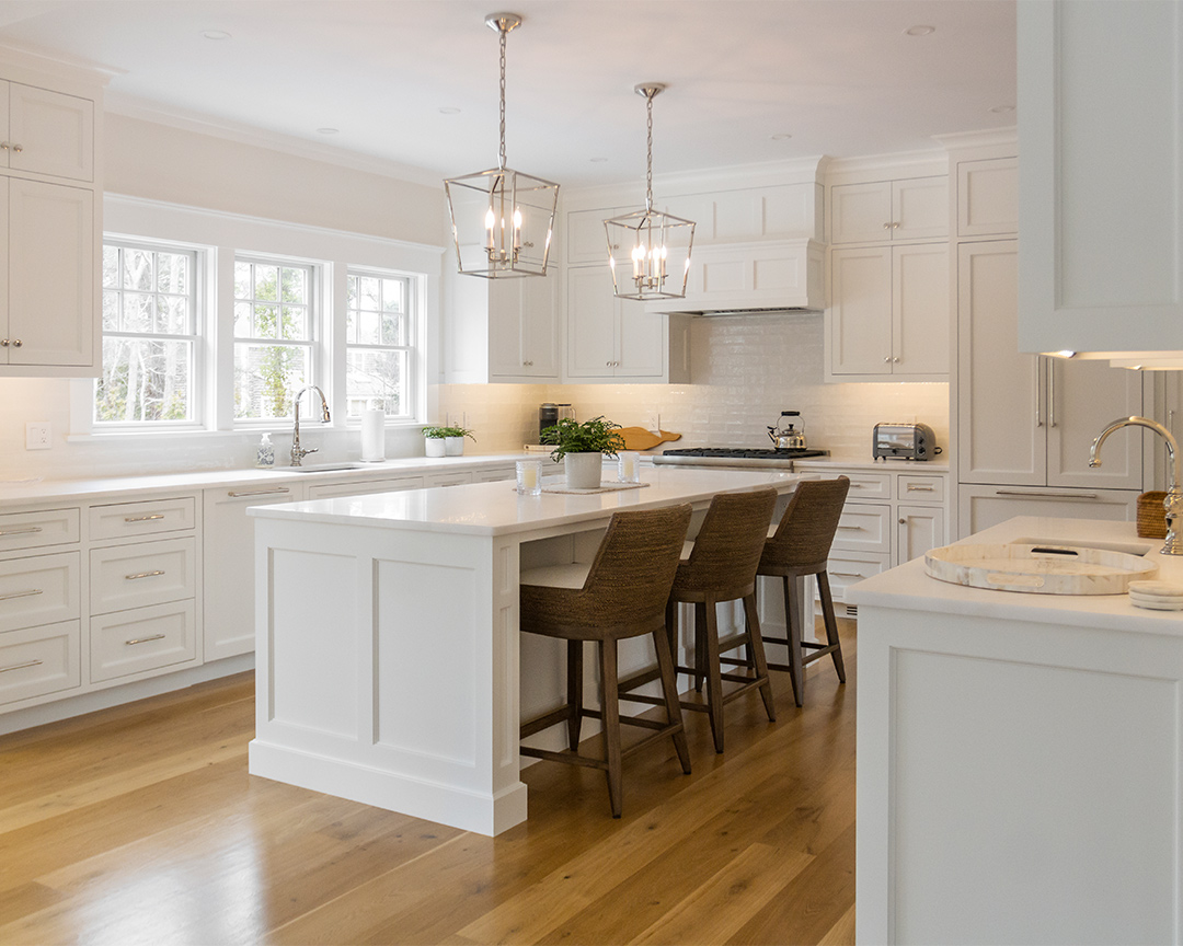 Modern kitchen with white cabinets, white island with dining chairs, and hardwood wide plank floors