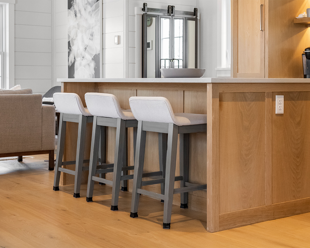 Unfinished wood flooring with wood colored island and modern style stools.