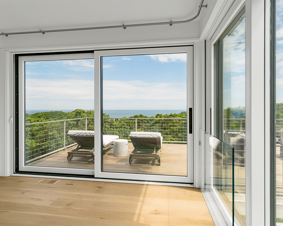 Light colored wood floors in room with large glass sliding doors overlooking beach horizon.