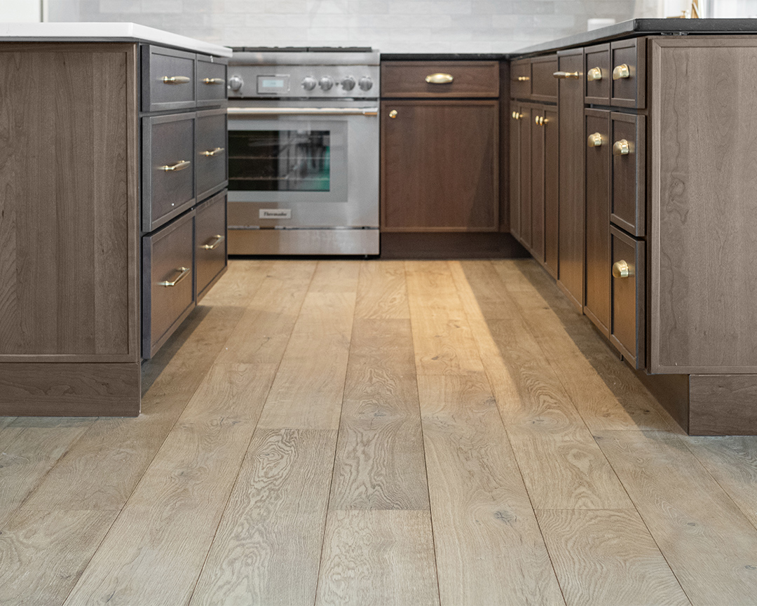 Close up of wood floor in kitchen with brown cabinets and visible oven