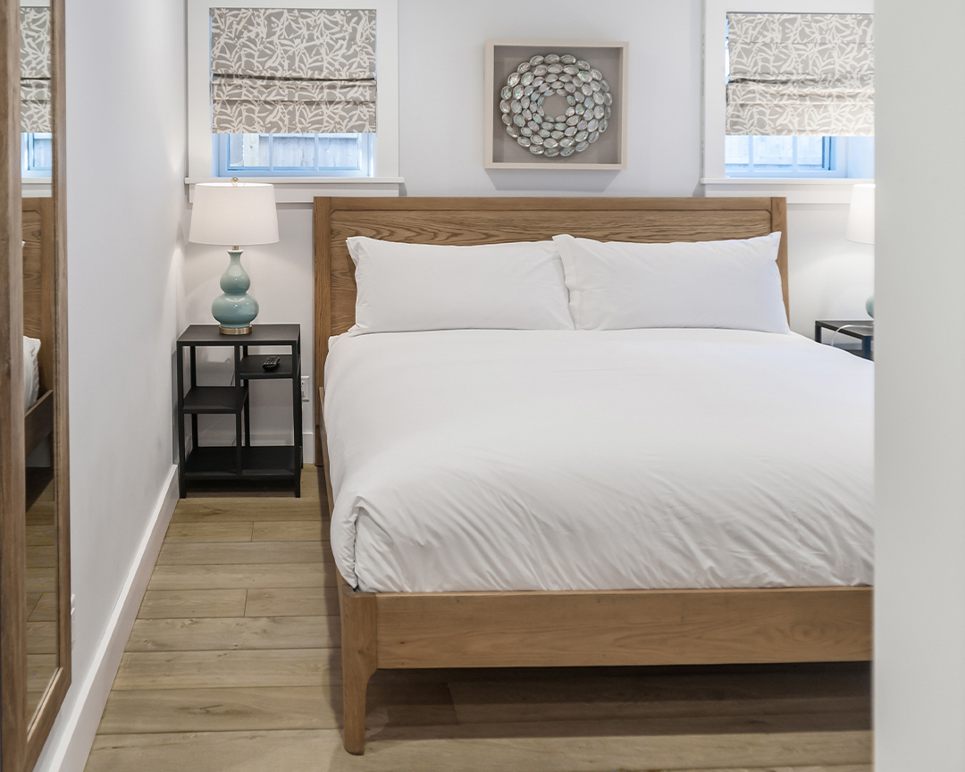 Bed with white sheets and clean decorations in a room with a french oak wood floor