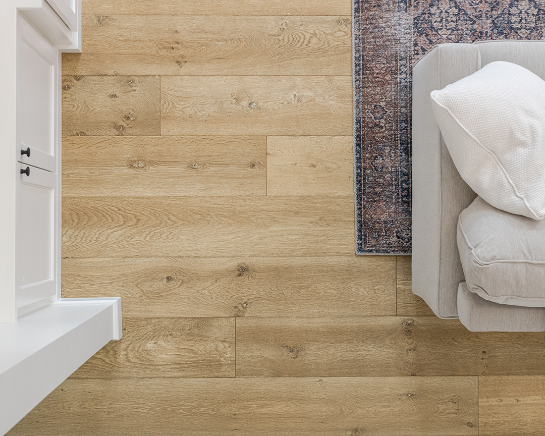 Top down shot of a white cabinet, beige couch, floral carpet, and a wide plank wood floor