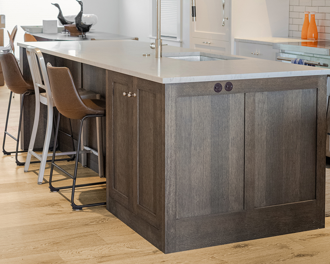 Close up of kitchen island with dark wood coloring, with dining chairs and a warm brown wood floor