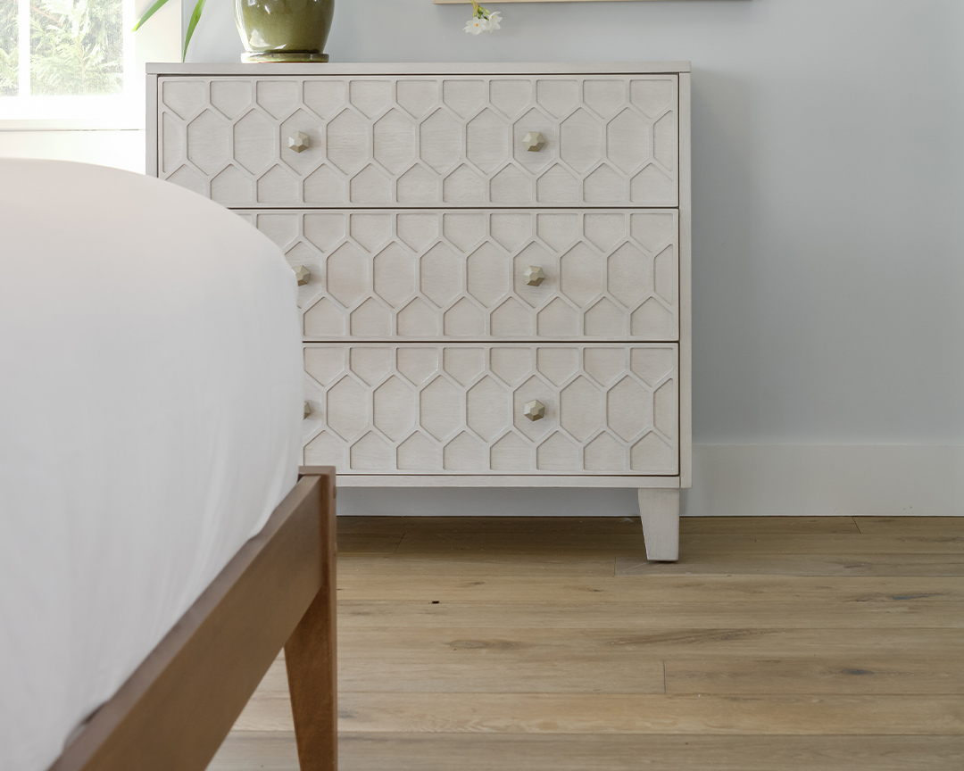 Close up of bedroom with wide plank flooring and white furniture