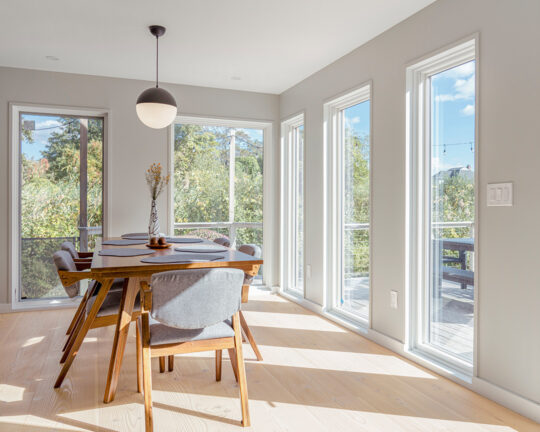 Sunny waterfront dining room with big windows and light wide plank wood flooring