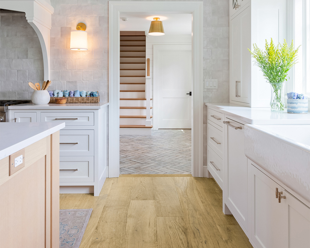 Close up of wood floor in modern kitchen with white cabinets and brown accents