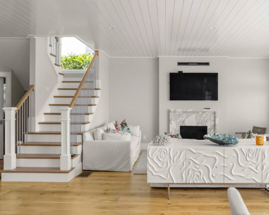 Soft, white living room design with stairs leading up to a sunny window juxtaposed to a rustic colored wood floor