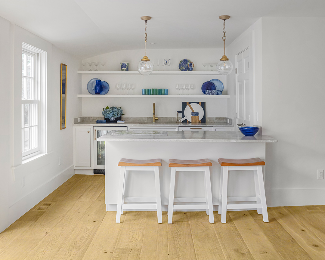 Coastal kitchen design with white cabinets, walls, and island, nestled on a wide plank wood floor