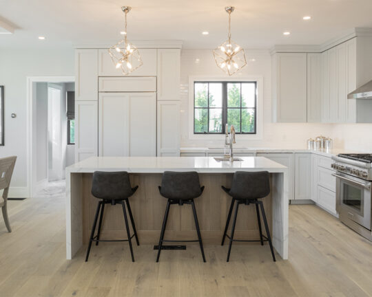 Kitchen with white cabinets and island with black dining chairs over a wide plank wood floor