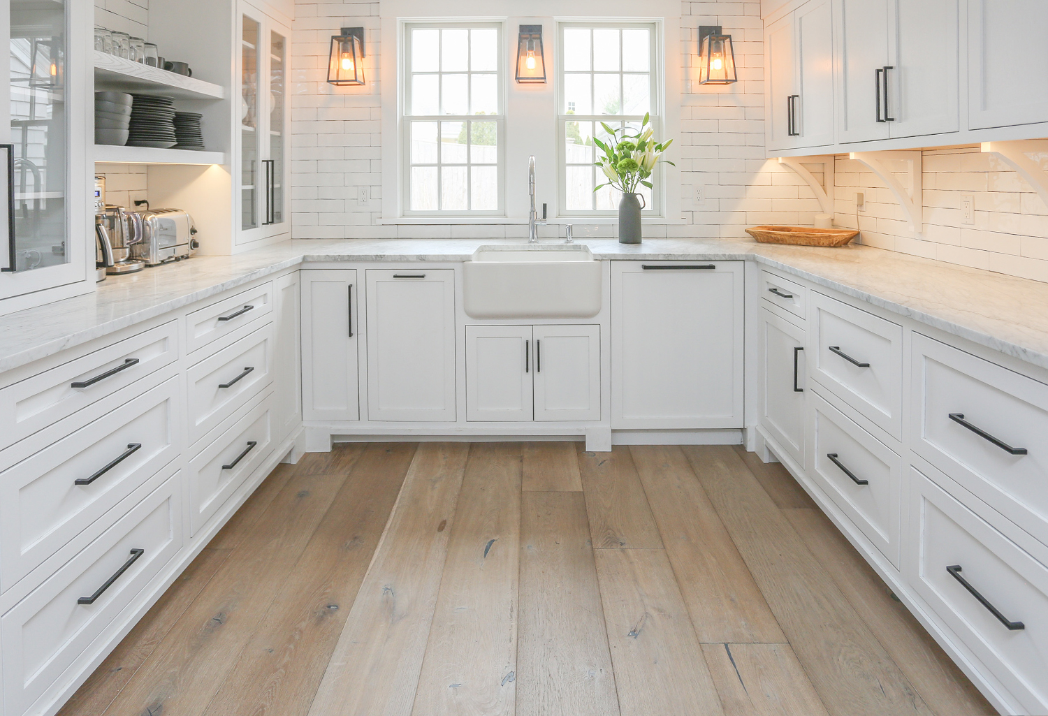 White kitchen cabinets and walls with wide plank wood flooring.