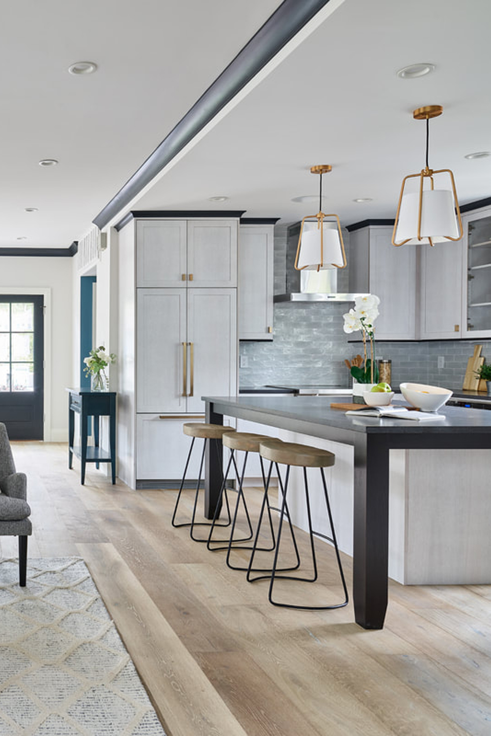 Diagonal shot of a luxury style kitchen and island with light brown wood flooring with gray hues.