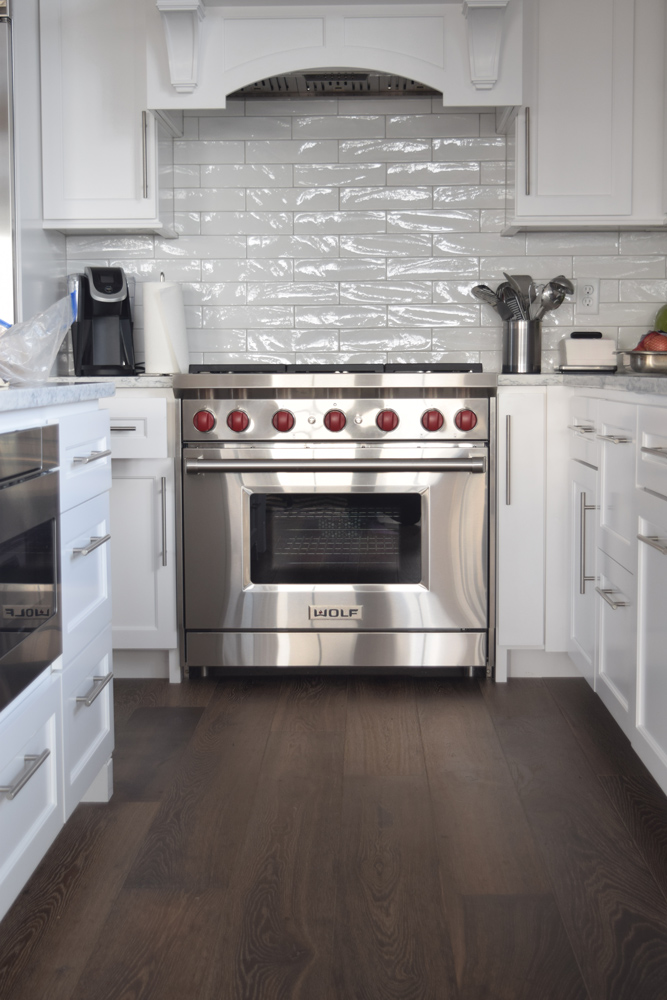 Dark brown wood flooring in a kitchen with white cabinets and shiny tiled backsplash.
