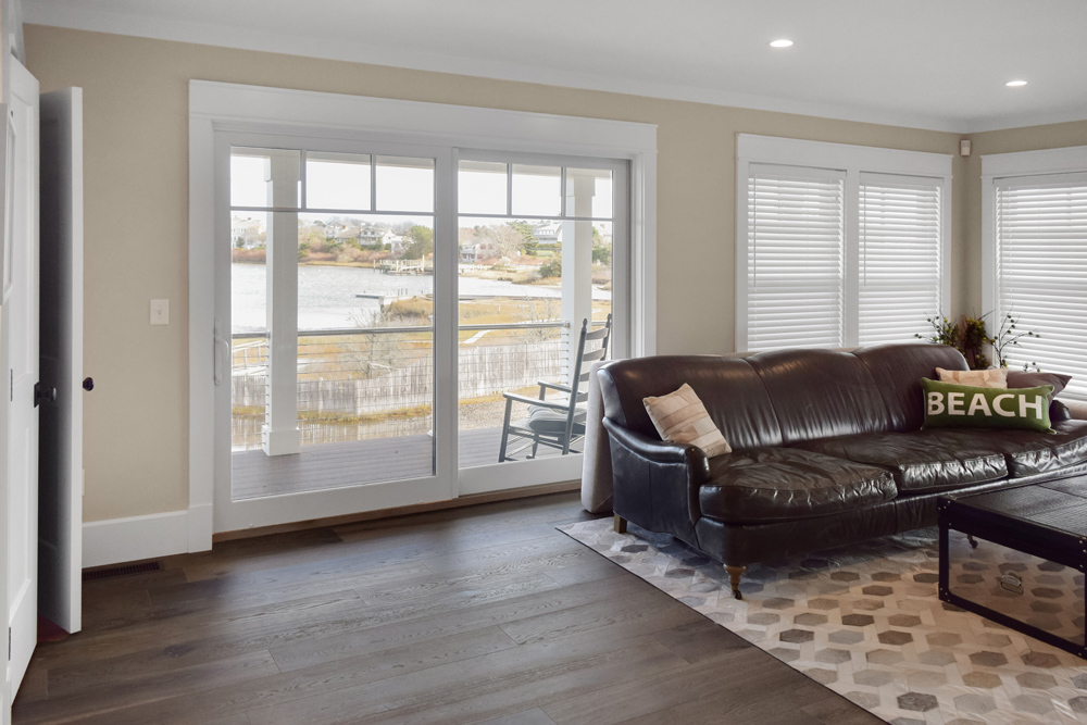 Coastal living room with ocean visible from sliding door, black leather couch, and dark brown wood flooring.