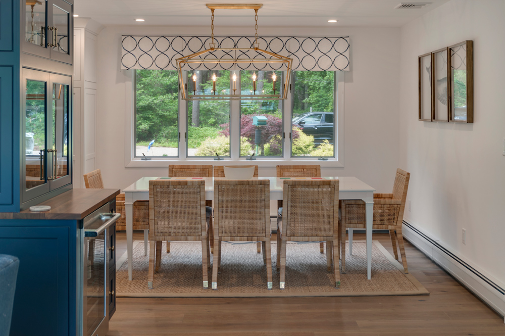 Dining area with large chandelier, greenery visible from windows, and a lightly distressed wood floor.