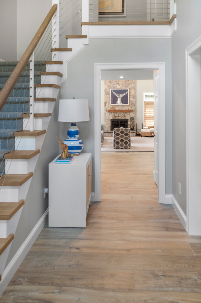 Hallway and staircase with living room and fireplace in distance, and a wood floor reminiscent of darkened driftwood.