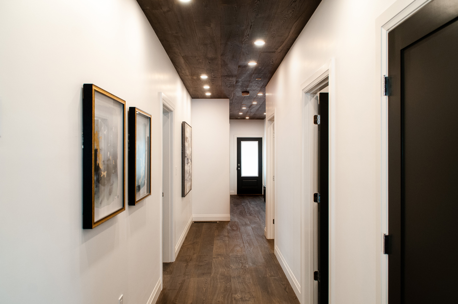 Hallway with dark wood paneled ceiling and dark wood floor with a modern aesthetic.