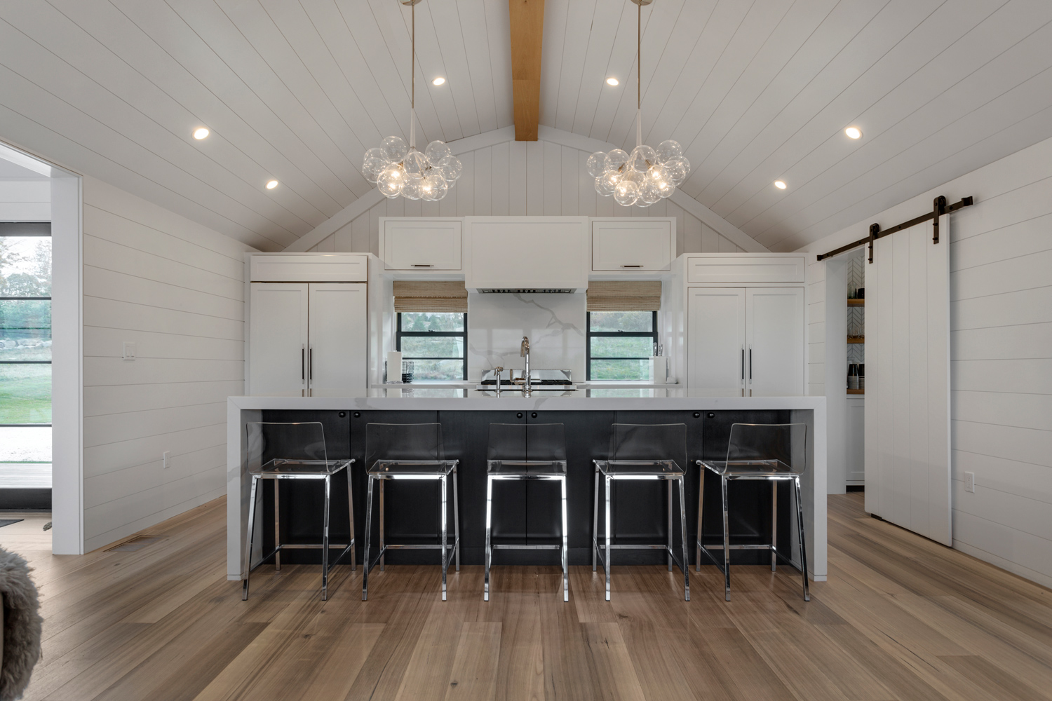 White colored kitchen with black accents, unique chandeliers, and wire-brushed wood flooring.
