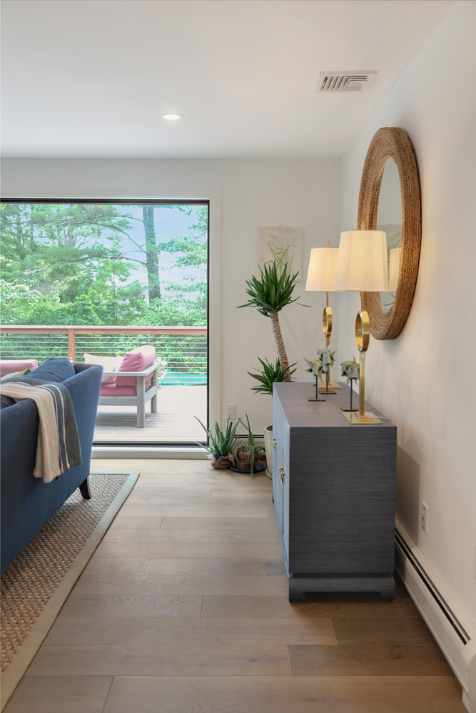 Coastal cottage with sunny windows and outdoor greenery and dark wood flooring.