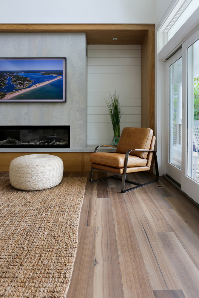 Modern living room with fireplace and lounge chair with stool and wide plank wood floor.