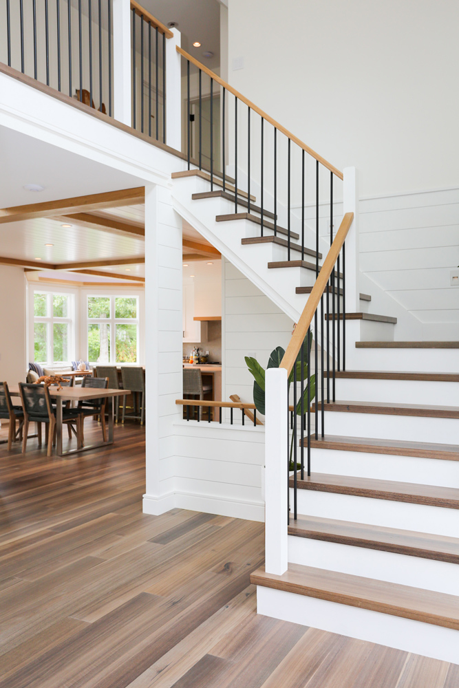 Staircase with dining room and kitchen in background with wire-brushed wood flooring.
