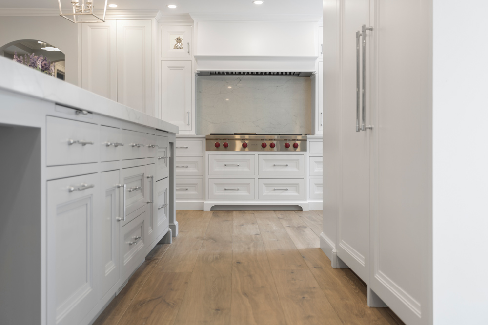 Brown wood flooring in kitchen with white cabinets.