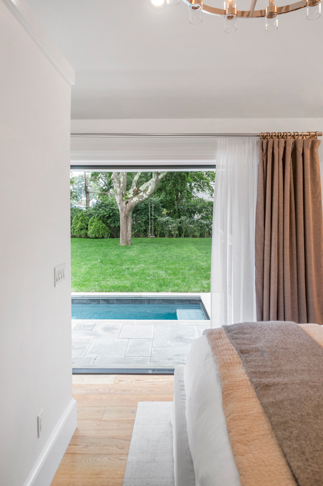 Bedroom with wood flooring and pool in view from glass door.