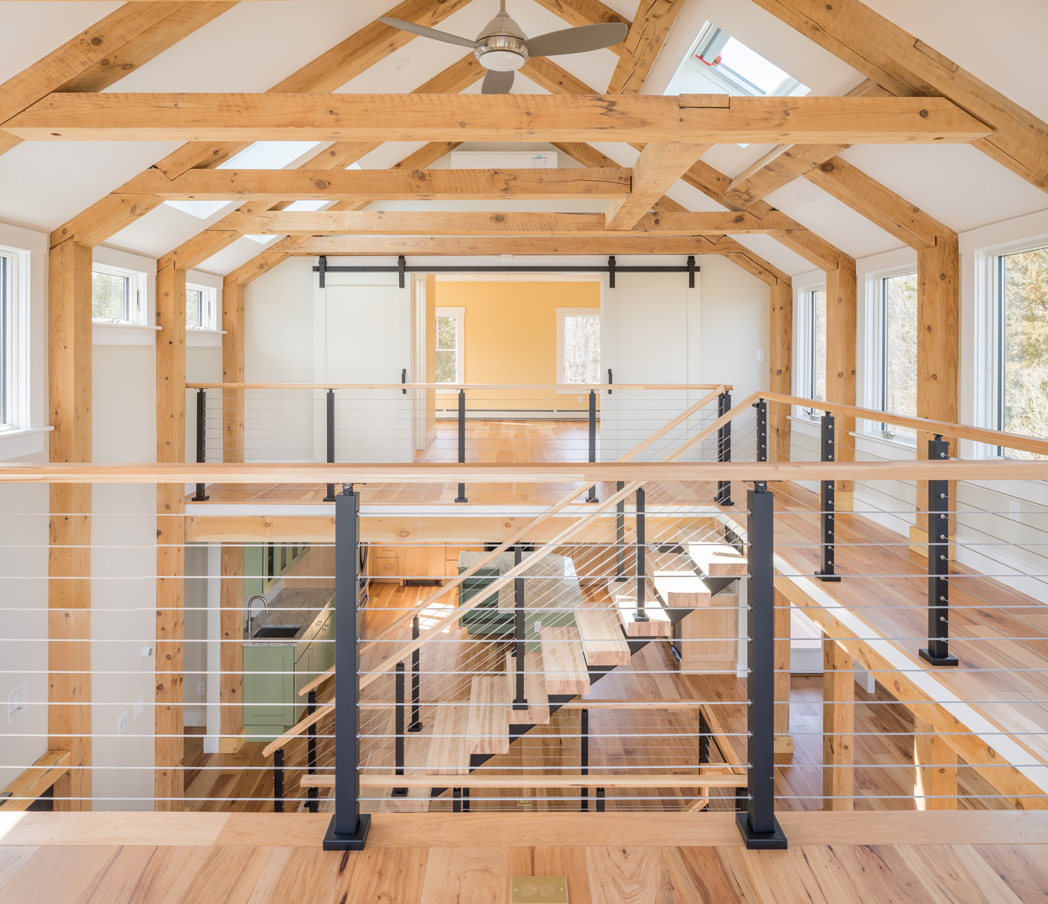 Bright, open, and unique loft design with stairs that match the flooring, high ceiling and wall beams, and a balcony overlooking first floor.