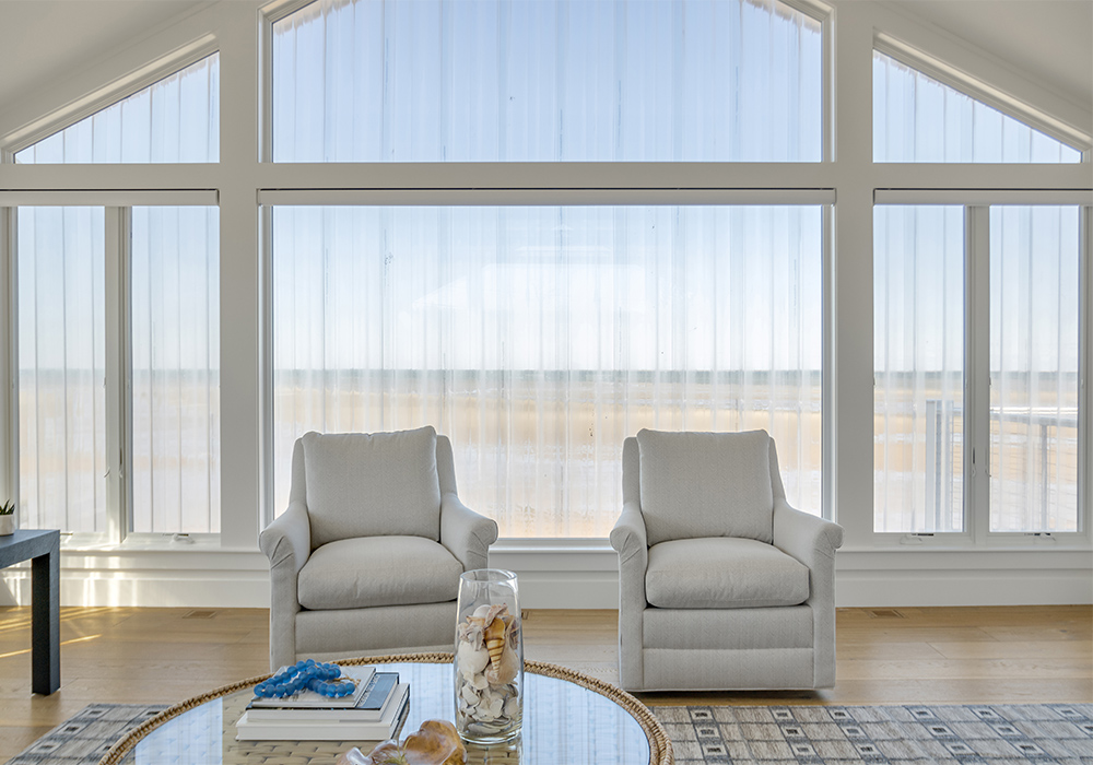 Coastal living room with large window wall, 2 armchairs, and a sunlit wood floor.