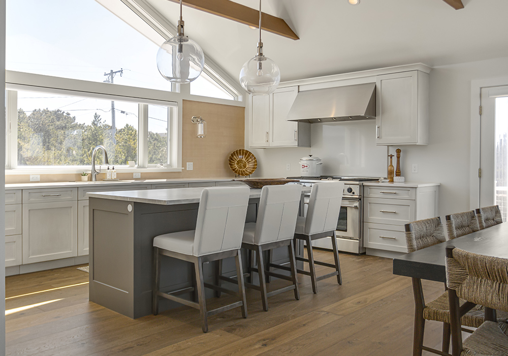 Modern kitchen with island and dining chairs with brown wood flooring.