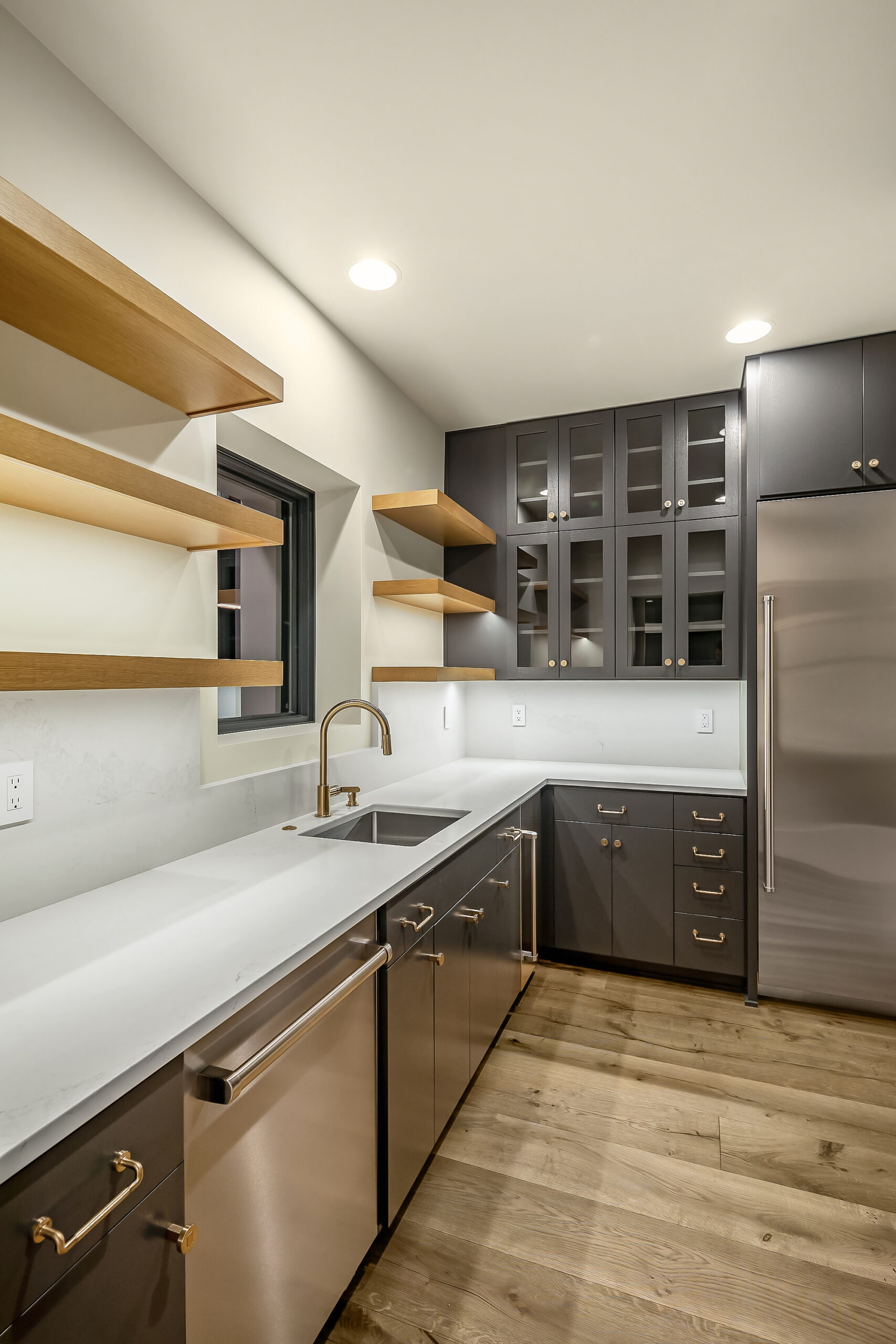 Modern kitchen design with floating shelves, gray cabinets, and rustic style wood floor.