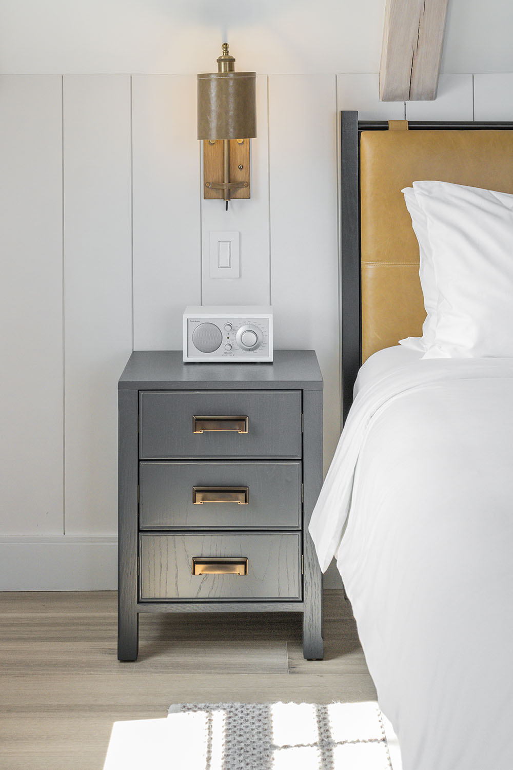 Bedroom with night table comprised of whites, grays, and browns with sunlit wood floor.