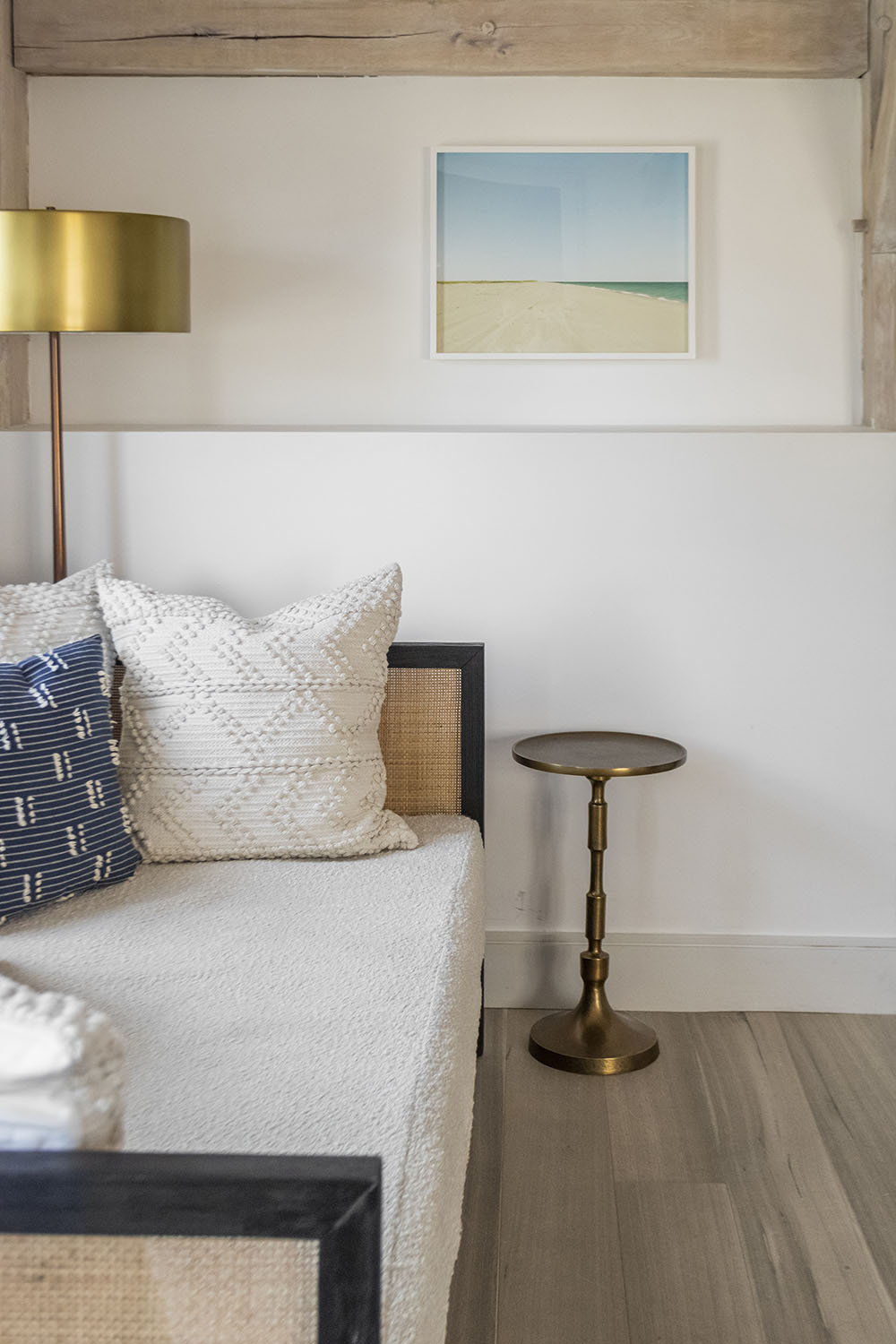 White couch and cushions with wall painting and brown and gray toned wood flooring.
