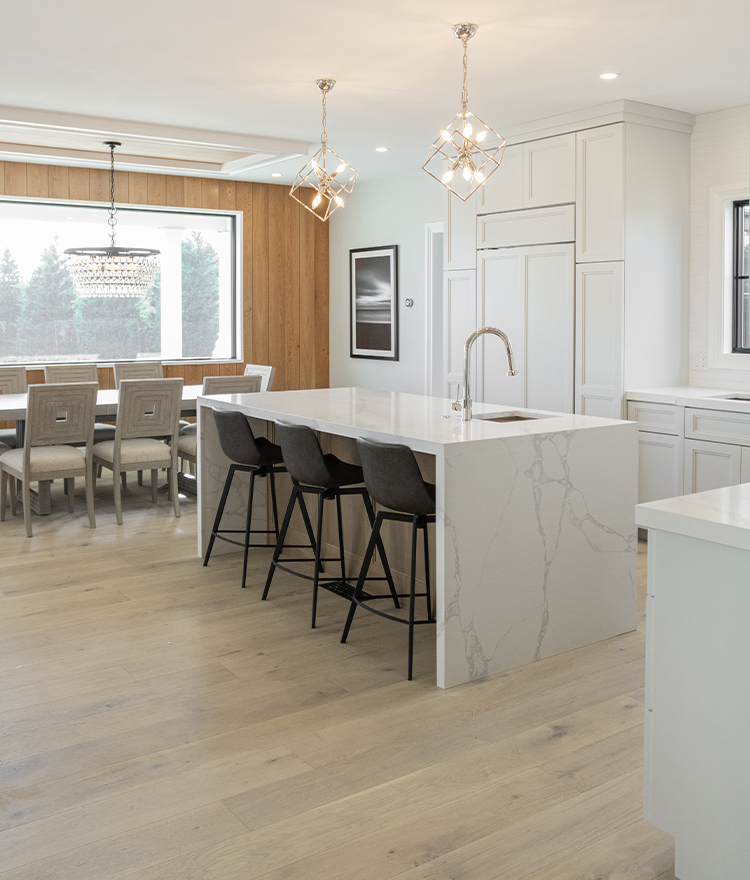 Modern kitchen with white marble island, cabinets, and wide plank oak wood flooring