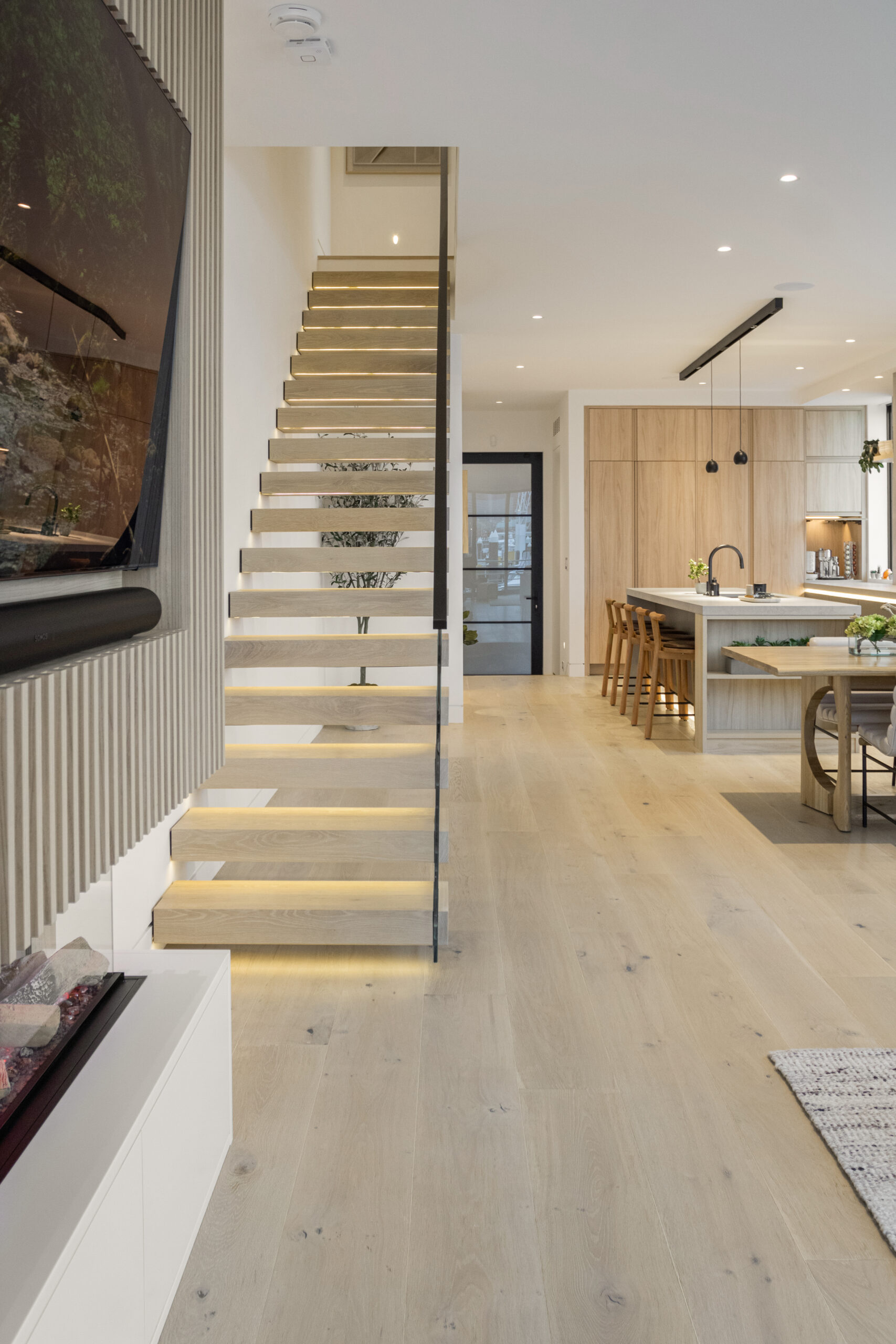 modern open floor plan kitchen and living room with floating stairs and light wide plank floors