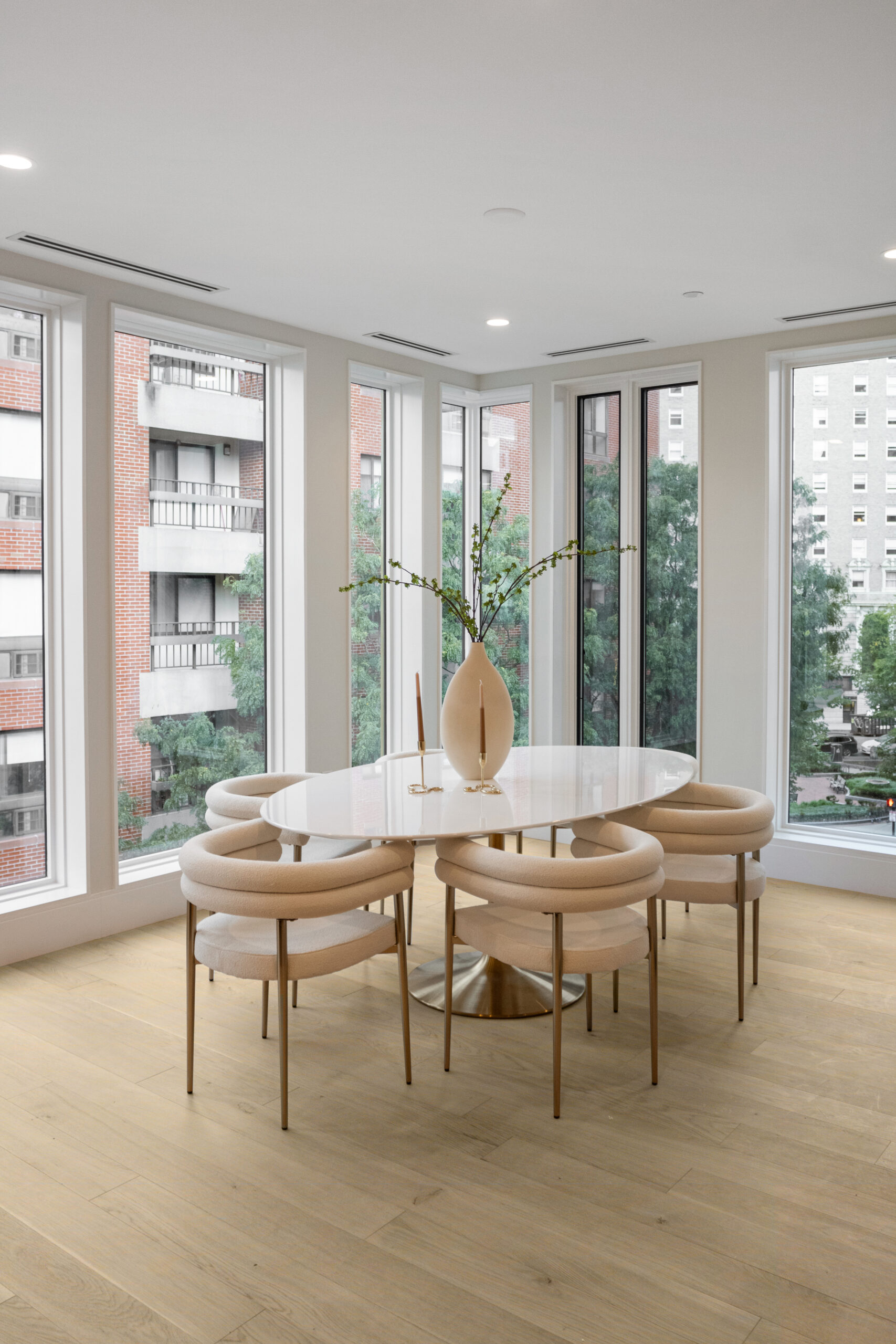 dining room in a corner surrounded by windows with neutral colored furniture and light wide plank floors